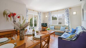 Un comedor con una mesa de madera dispuesta para dos personas, un sofá y un televisor al fondo.
