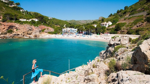 Eine Küstenlandschaft mit Strand, felsigen Klippen und Gebäuden im Hintergrund.