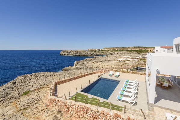 A pool area with lounge chairs, a clear view of the sea, and rocky terrain. - Villa Agata by Villa Plus (Los Delfines)