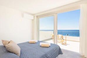 A bedroom with a large bed, a balcony with a view of the sea, and a chair. - Villa Agata by Villa Plus (Los Delfines)