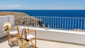 Ein Balkon mit Meerblick, eine Champagnerflasche und ein Strohhut auf einem Stuhl.