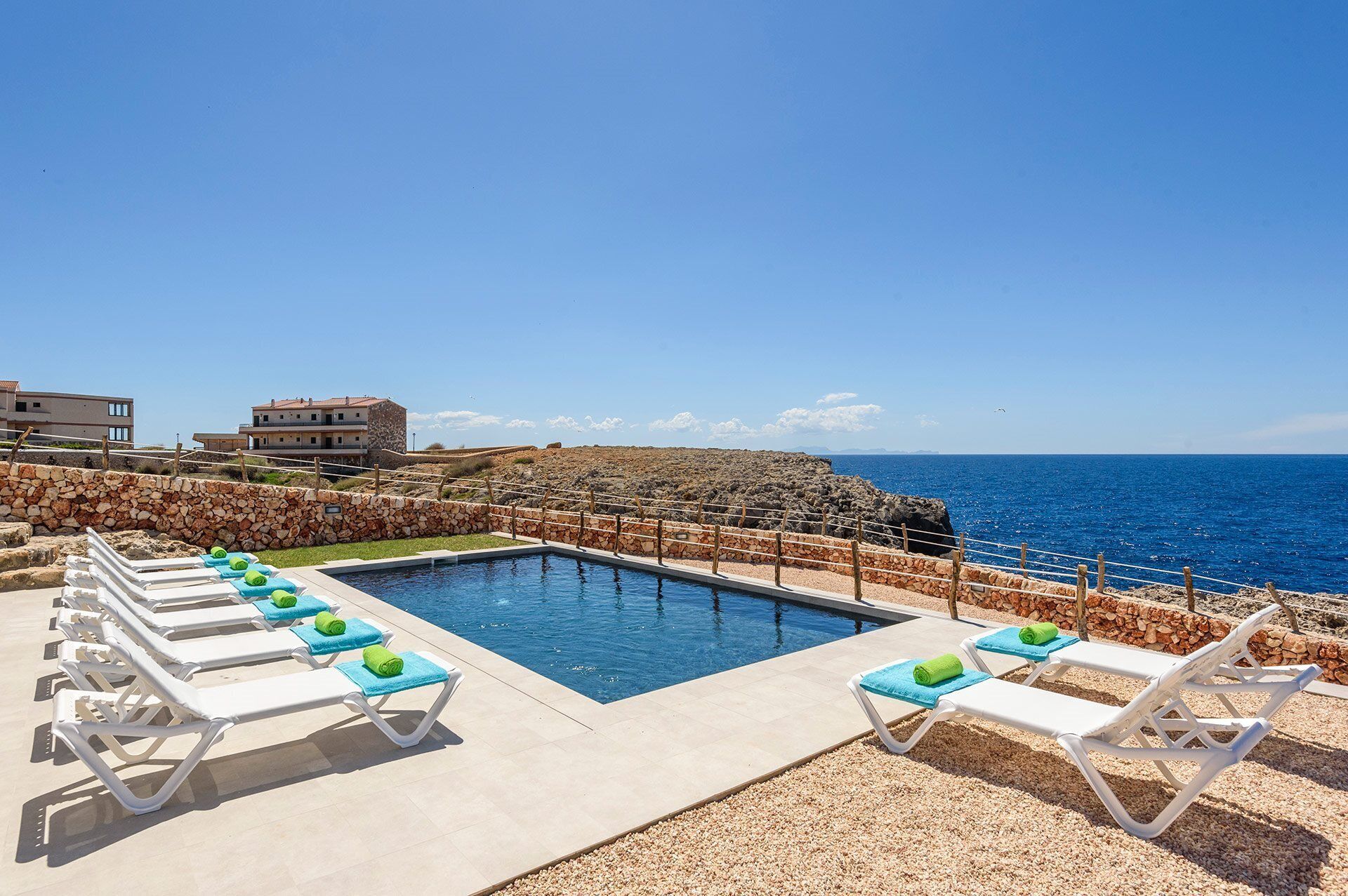 Zona junto a la piscina con sillas de descanso y vista despejada al mar.