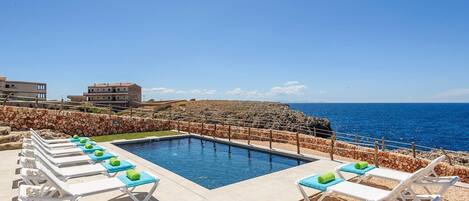 Zona junto a la piscina con sillas de descanso y vista despejada al mar.