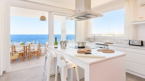Eine moderne Küche mit einer großen Kochinsel, ein Essbereich mit Meerblick und ein Balkon mit Sitzgelegenheit.