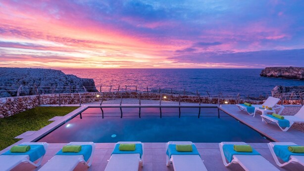 Ein Poolbereich mit Liegestühlen und Blick auf das Meer bei Sonnenuntergang.