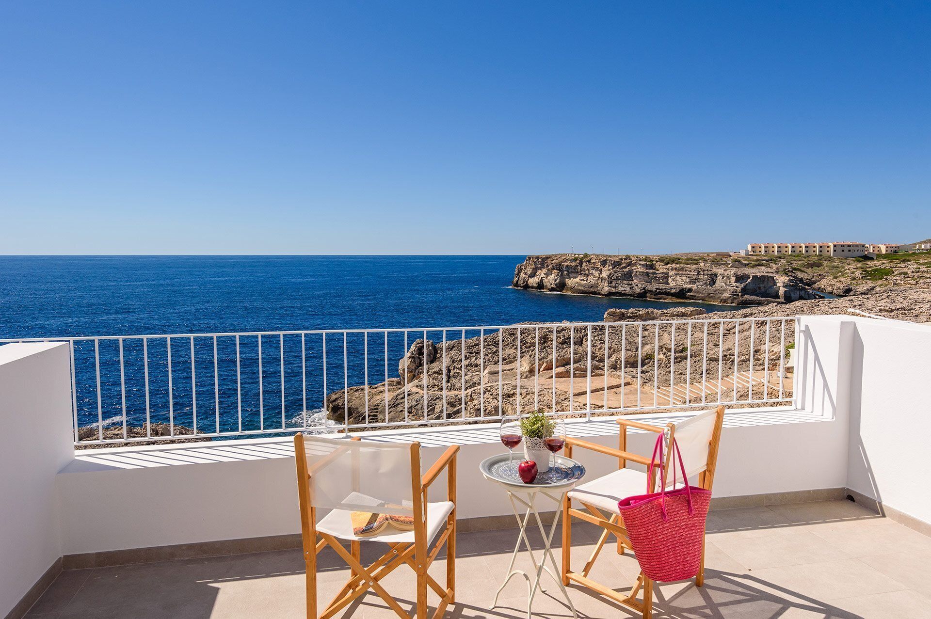 Un balcón con vista al mar, una mesa con sillas y un bolso rojo.