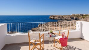 Een balkon met uitzicht op zee, een tafel met stoelen en een rode tas.