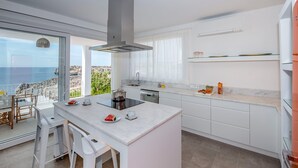 Een moderne keuken met een groot eiland, witte kastjes en uitzicht op zee.