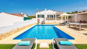 Piscina com cadeiras de praia e um edifício ao fundo.