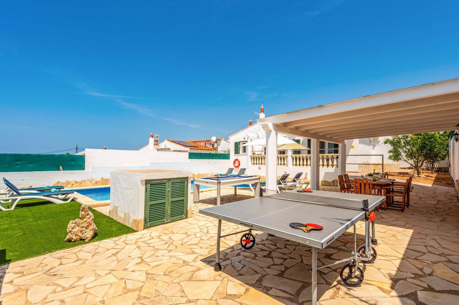A pool area with lounge chairs, a ping pong table, and a view of the sea.