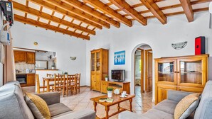 Uma sala de estar ampla com teto de madeira, uma mesa de jantar com cadeiras, uma TV e um armário com portas de vidro.