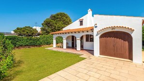 A white building with a tiled roof, a wooden door, and a paved driveway. - Villa Aljub by Villa Plus (Ciutadella de Menorca)