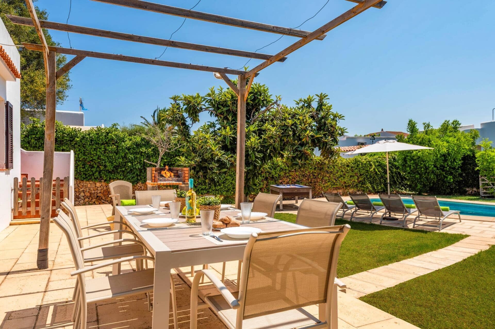 An outdoor patio with a table set for dining, surrounded by chairs, a grill, and a pool area with lounge chairs.