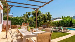 An outdoor patio with a table set for dining, surrounded by chairs, a grill, and a pool area with lounge chairs. - Villa Aljub by Villa Plus (Ciutadella de Menorca)