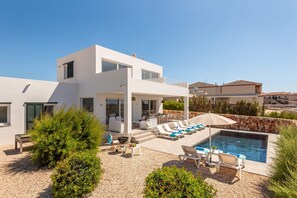 A modern two-story house with a pool, outdoor seating, and a stone wall.