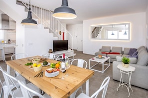 A modern living space with a dining area, a sofa, and a staircase.