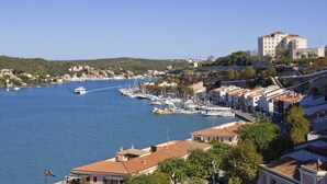 A coastal town with a marina filled with boats, a prominent building on a hill, and residential buildings along the waterfront. - Villa Amatista by Villa Plus (Los Delfines)