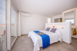 A modern bedroom with a bed, a built-in bedside table, and a large window.