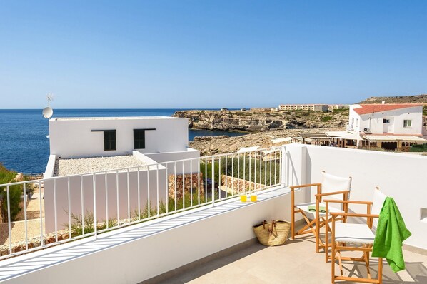 A terrace with a view of the sea, white buildings, and a rocky coastline.