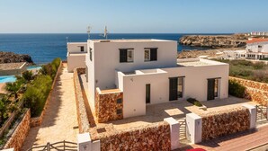 A modern white building with a stone foundation, a pool, and a view of the sea. - Villa Amatista by Villa Plus (Los Delfines)