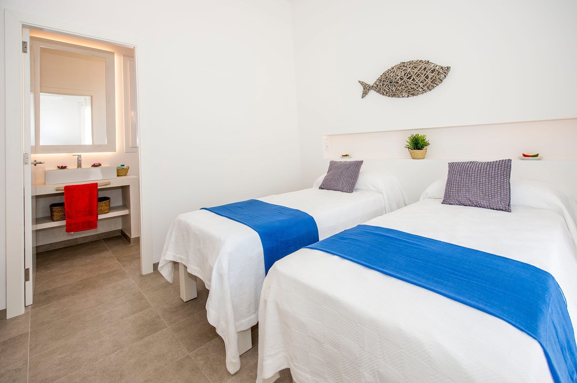 Habitación de hotel con dos camas, un lavamanos blanco, un espejo y una decoración de peces colgada en la pared.
