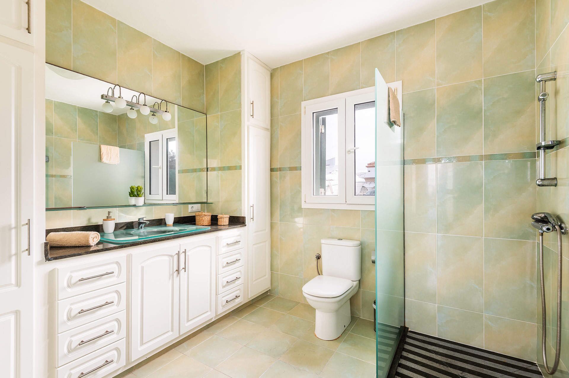 Un baño con cabina de ducha de vidrio, inodoro y lavamanos con espejo.
