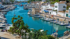 Ein Yachthafen mit zahlreichen Booten, die an einem schmalen Kanal liegen, umgeben von Gebäuden im mediterranen Stil.