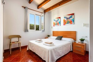 A bedroom with a bed, a nightstand, a chair, and two paintings on the wall.