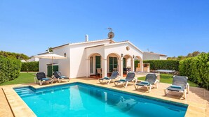 A pool area with lounge chairs and a building with arches. - Villa Avellano by Villa Plus (Cap d'Artrutx)