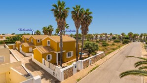 Una villa gialla con tetto in tegole, circondata da palme e un cielo sereno.