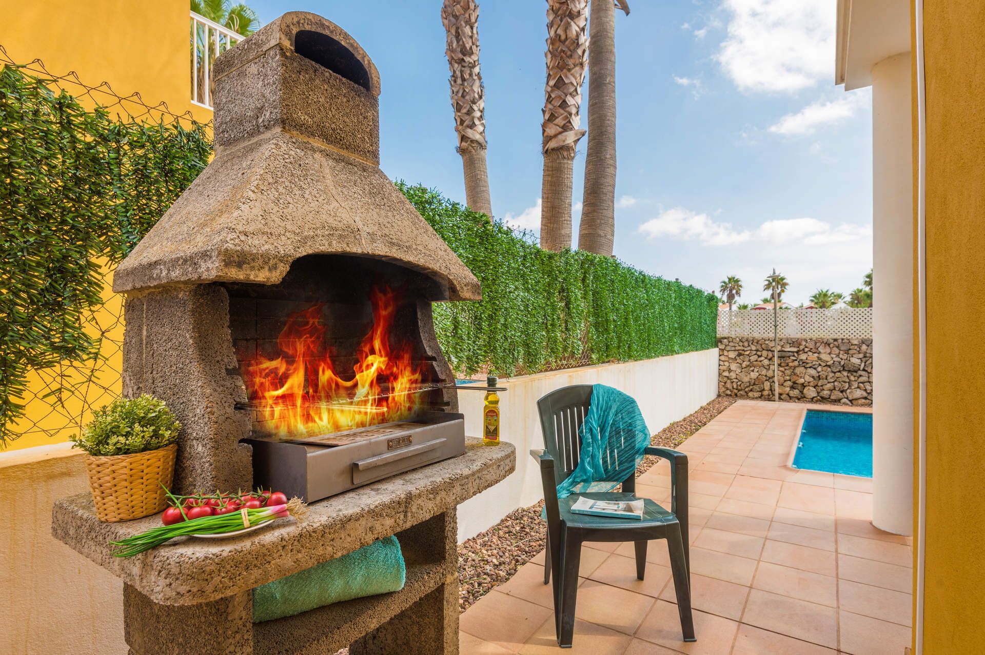 Un horno de piedra al aire libre con llamas, una piscina y una silla.