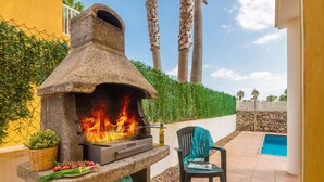 Forno in pietra all'aperto con fiamme, una piscina e una sedia.