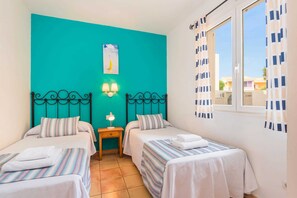 A room with two beds, teal walls, a window with curtains, and a painting on the wall.