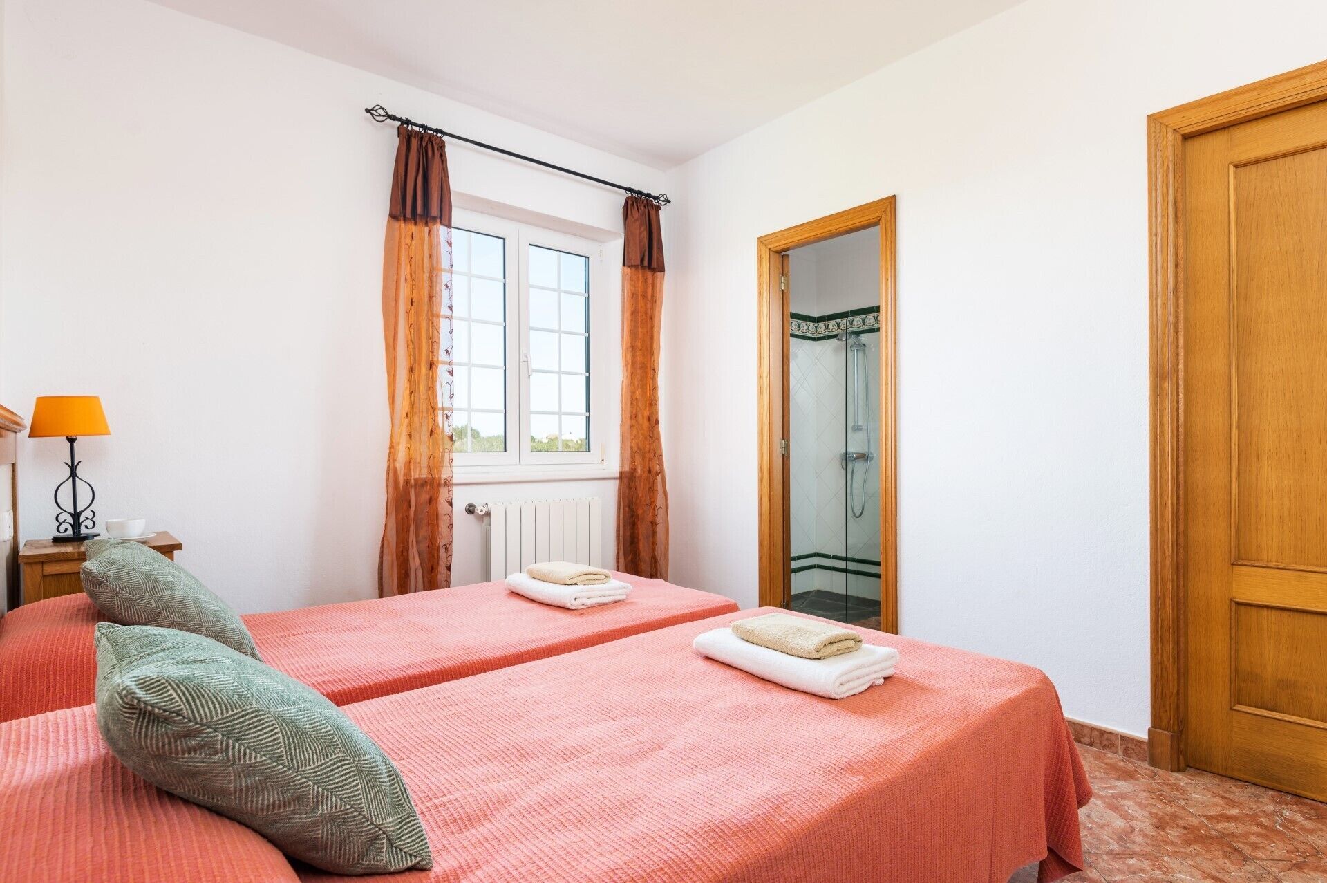 A hotel room with two beds, a window with curtains, a wooden door, and a mirror.