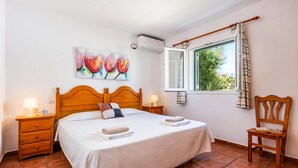 Una camera da letto ordinata con un letto, comodini, una sedia, una finestra con tende e un quadro appeso al muro.