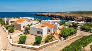 Una zona residenziale sul lungomare, con edifici bianchi e tetti arancioni, immersa nel verde e affacciata su scogliere rocciose.