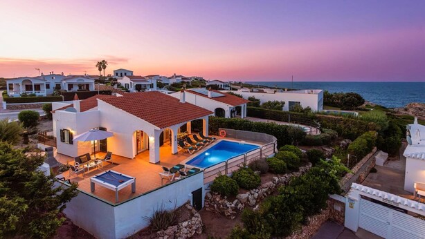 Una villa moderna con piscina, area relax esterna e vista sul mare al tramonto.