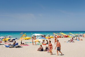 A beach with sun loungers, umbrellas, and people relaxing.