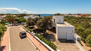 En modern vit byggnad med ett platt tak, ett takförsett parkeringsområde och utsikt över havet.