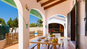Patio esterno con tavolo in legno apparecchiato per mangiare, parete in pietra e vista sulla zona piscina.