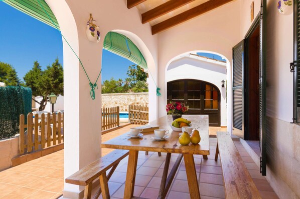 An outdoor patio with a wooden table set for dining, a stone wall, and a view of the pool area.