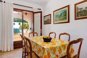 A dining area with a table set for four, surrounded by wooden chairs. There are three framed paintings on the wall above the table.