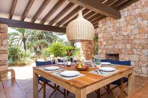 An outdoor dining area with a wooden table set for four, surrounded by stone walls and a hanging wicker light fixture. - Villa Diamante by Villa Plus (Sant Lluís)