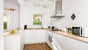 Une cuisine moderne avec des armoires blanches, un plan de travail en bois, un four encastré, un four à micro-ondes et une fenêtre donnant sur un espace verdoyant.