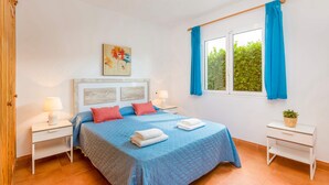 A bedroom with a bed, two bedside tables, a window with curtains, a painting on the wall, and a potted plant. - Villa Dolfi by Villa Plus (Los Delfines)