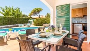 An outdoor dining area with a pool, wicker chairs, and a table set for a meal. - Villa Dolfi by Villa Plus (Los Delfines)