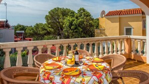 Une terrasse avec une table dressée pour le dîner, entourée de chaises en osier, et offrant une vue sur un paysage verdoyant et luxuriant.