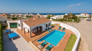 Eine weiße Villa mit Swimmingpool, Sitzgelegenheiten im Freien und Meerblick.