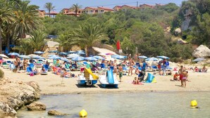 Una playa con muchos sombrillas, gente y barcos.