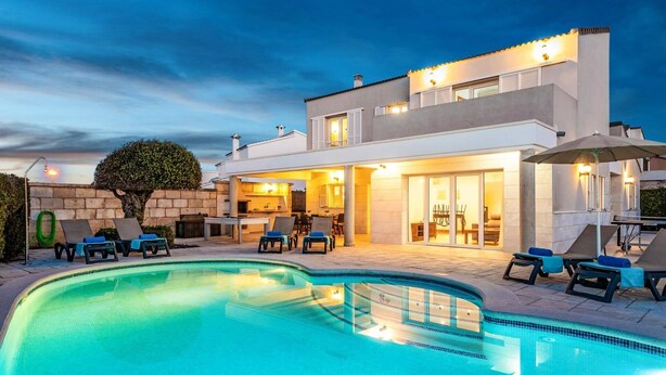 Una casa moderna de dos pisos con piscina, mobiliario de exterior y un patio bien iluminado.